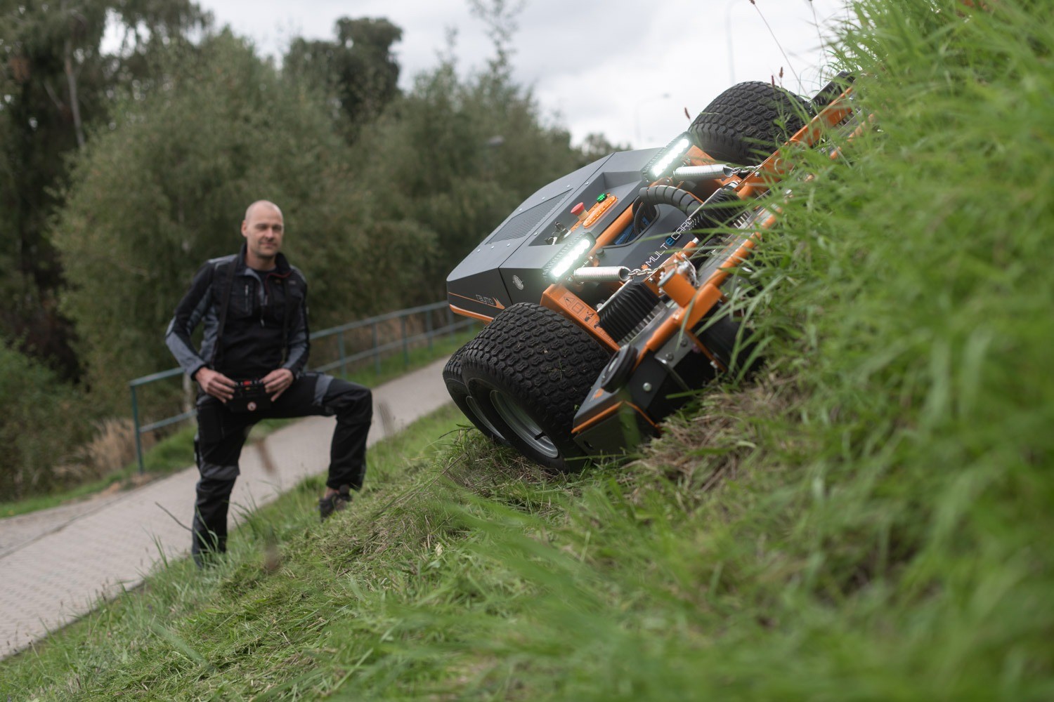 Raymo hero RAYMO remote-controlled mower on a steep grass bank with its operator